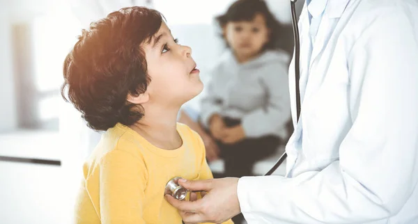 Güneşli klinikte bir çocuk hastayı steteskopla muayene eden kadın doktor. Hekim randevusunda tatlı Arap çocuk. — Stok fotoğraf