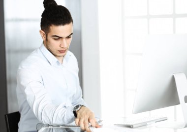 İşadamı modern ofiste bilgisayarla çalışıyor. Arap erkek girişimcinin iş yerindeki portresi. İş konsepti