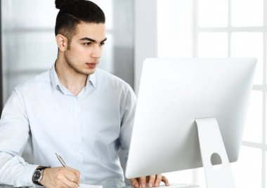 İşadamı modern ofiste bilgisayarla çalışıyor. Arap erkek girişimcinin iş yerindeki portresi. İş konsepti