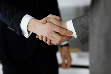 Bilinmeyen işadamı, modern ofiste dikilirken iş arkadaşı ya da ortağıyla el sıkışıyor. Toplantıda iş adamları grubu