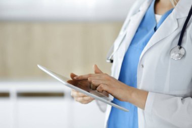 Bilinmeyen kadın doktor klinikte duruyor ve tablet bilgisayar kullanıyor, yakın plan. Tıp ve sağlık alanlarındaki veriler