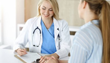 Kadın doktor ve hasta güneşli klinikte oturup konuşuyor. Sarışın terapist neşeyle gülümsüyor.