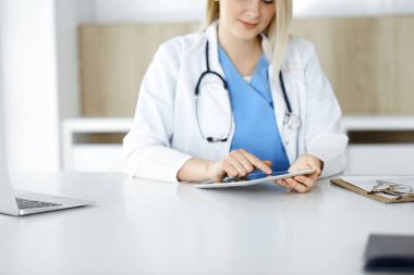 Bilinmeyen kadın doktor klinikte duruyor ve tablet bilgisayar kullanıyor, yakın plan. Veriler ve tıp ve sağlık hizmetlerindeki en iyi hizmet