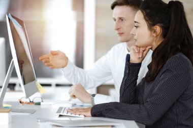 İş kadını ve erkek, güneşli ofiste bilgisayar kullanırken soruları tartışıyorlar.