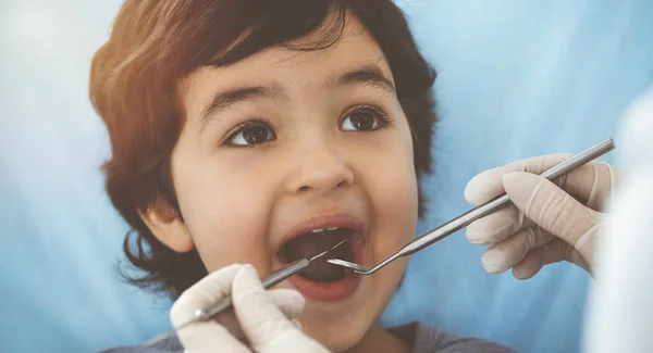 Lindo chico árabe sentado en la silla dental con la boca abierta durante el control oral con el médico. Visita al soleado consultorio del dentista — Foto de Stock