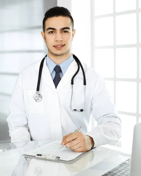 Homem médico árabe está usando computador portátil ao preencher registros de histórico de medicação na mesa de vidro na clínica r. Conceito de medicina — Fotografia de Stock