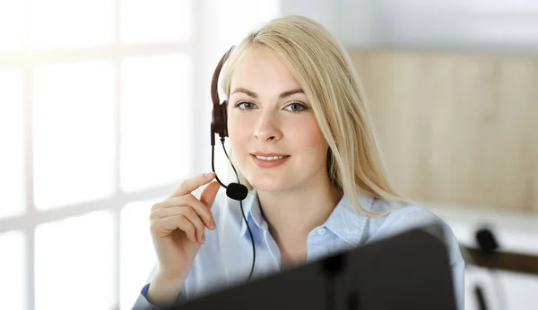 Blonde business woman sitting and communicated by headset in call center in sunny office. Concept of telesales business — Stock Photo, Image