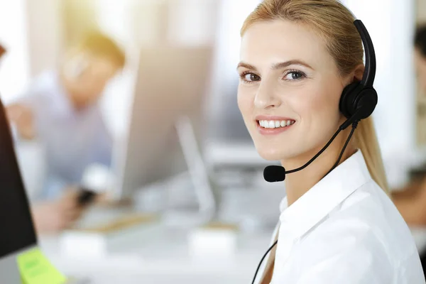 Donna d'affari bionda che usa le cuffie per comunicare e consultare la gente all'ufficio soleggiato. Call center — Foto Stock