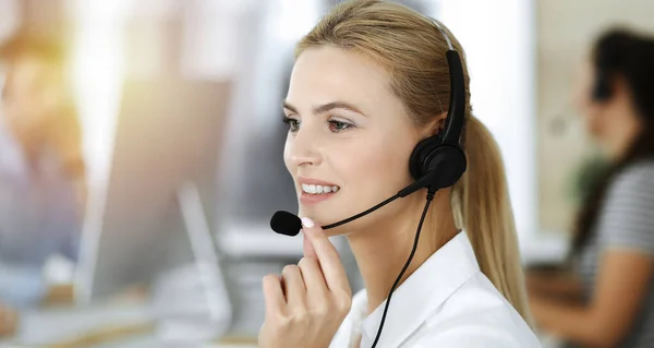 Mujer rubia de negocios que usa auriculares para comunicarse y consultar a la gente en la oficina soleada. Centro de llamadas — Foto de Stock