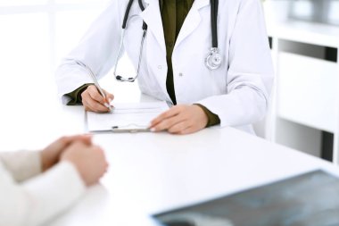 Kadın doktor ve hasta hastane muayenehanesinde oturuyor ve konuşuyor, yakın plan. İlaç kayıtlarını dolduran bir terapist. Tıp ve sağlık hizmetleri kavramı