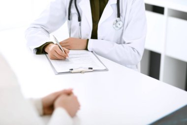 Kadın doktor ve hasta hastane muayenehanesinde oturuyor ve konuşuyor, yakın plan. İlaç kayıtlarını dolduran bir terapist. Tıp ve sağlık hizmetleri kavramı