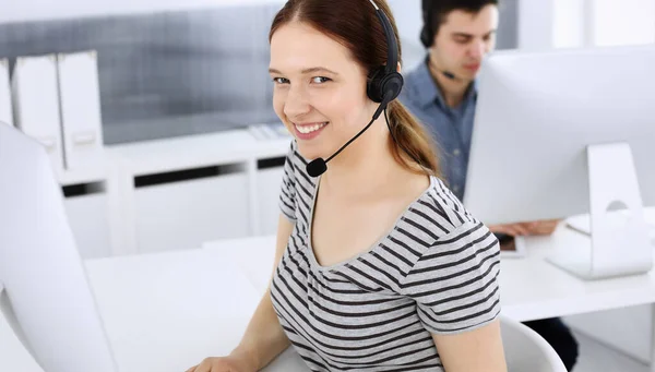 Grupo de operadores en el trabajo. Centro de llamadas. Enfócate en la hermosa recepcionista en auriculares al servicio al cliente. Concepto de negocio y estilo casual de ropa a rayas — Foto de Stock