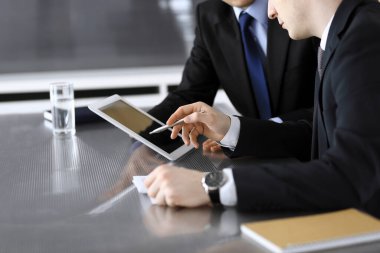 İşadamı tablet bilgisayar kullanıyor ve iş arkadaşı ya da ortağıyla modern ofiste cam masada çalışıyor. Yakın plan. Toplantıda bilinmeyen iş adamları var. Takım çalışması ve ortaklık kavramı