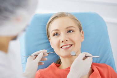 Gülümseyen beyaz kadın dişçi kliniğinde dişçi tarafından muayene ediliyor. Sağlıklı dişler ve ilaçlar, stomatoloji konsepti