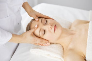 Güzel beyaz kadın spa salonunda gözleri kapalı yüz masajından zevk alıyor. Tıp ve Güzellik konseptinde rahatlatıcı tedavi