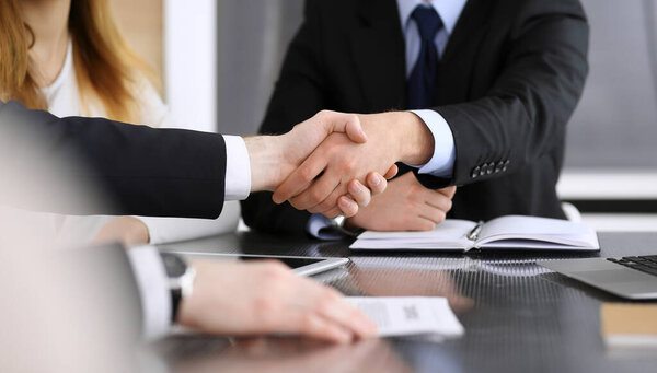 Businessman shaking hands with his colleague or partner above the glass desk in modern office, close-up. Unknown business people at meeting. Teamwork, partnership and handshake concept