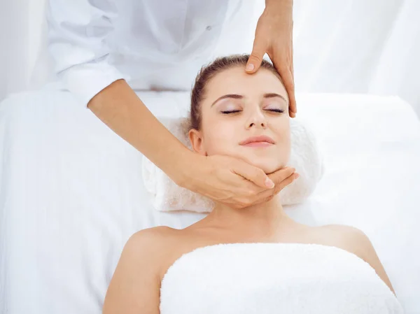 Young and blonde woman enjoying facial massage in spa salon. Beauty concept — Stock Photo, Image