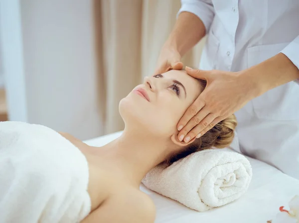 Jonge en blonde vrouw geniet van gezichtsmassage in spa salon. Schoonheidsconcept — Stockfoto