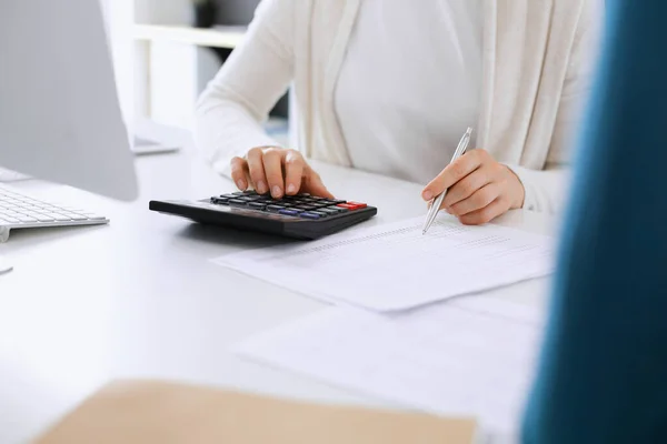 Accountant checking financial statement or counting by calculator income for tax form, hands closeup. Business woman sitting and working with colleague at the desk in office. Tax and Audit concept