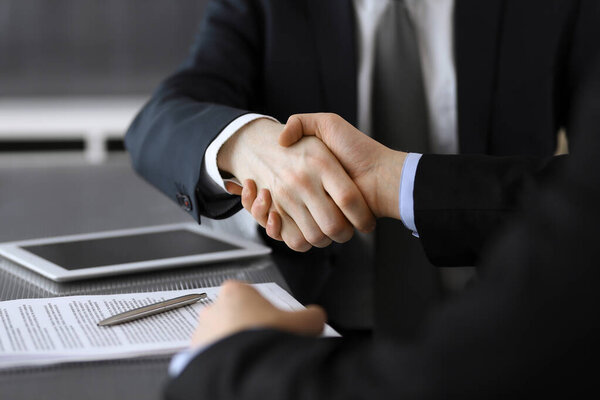Бизнесмен пожимает руку коллеге или партнеру над стеклянным столом в современном офисе крупным планом. Неизвестные бизнесмены на встрече. Командная работа, партнерство и концепция рукопожатия