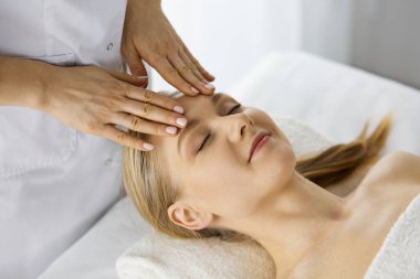 Güzel beyaz kadın spa salonunda gözleri kapalı yüz masajından zevk alıyor. Tıp ve Güzellik konseptinde rahatlatıcı tedavi