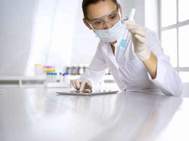 Kadın laboratuvar asistanı mavi sıvıyla test tüpünü analiz ediyor. Tıp, sağlık ve araştırma konsepti