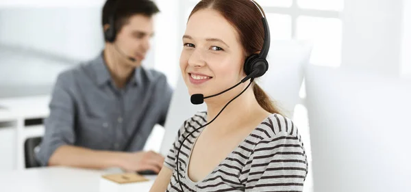 Mujer joven vestida casual usando auriculares y computadora mientras habla con los clientes en línea. Grupo de operadores en el trabajo. Call center, concepto de negocio —  Fotos de Stock