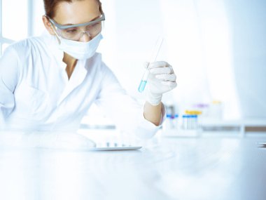 Kadın laboratuvar asistanı mavi sıvıyla test tüpünü analiz ediyor. Tıp, sağlık ve araştırma konsepti