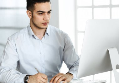 İşadamı modern ofiste bilgisayarla çalışıyor. Arap erkek girişimcinin iş yerindeki portresi. İş konsepti