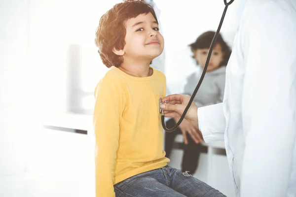 Mujer-médico examinando a un niño paciente por estetoscopio en el soleado Clinik. Lindo chico árabe en la cita con el médico — Foto de Stock