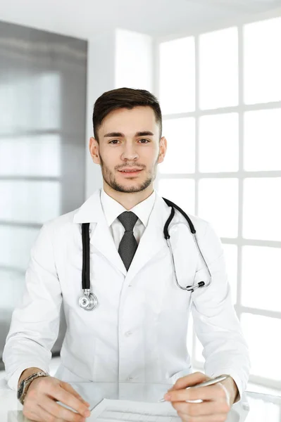 Läkaren fyller i journaler när han sitter vid skrivbordet på kliniken. Medicin och hälsovård — Stockfoto