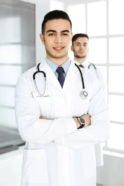 Arabski lekarz stojący z białym kolegą w gabinecie medycznym lub klinice. Różnorodny zespół lekarzy, koncepcja medycyny i opieki zdrowotnej — Zdjęcie stockowe