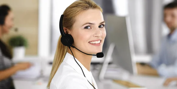 Mujer rubia de negocios con auriculares para la comunicación y la consulta de las personas en la oficina de servicio al cliente. Centro de llamadas. Grupo de operadores en el trabajo — Foto de Stock