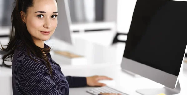 Бізнес-жінка використовує комп'ютер на робочому місці в сучасному офісі. Секретарка Брюнета або жінка-адвокат посміхається і виглядає щасливою. Праця за розвагами і успіхом — стокове фото