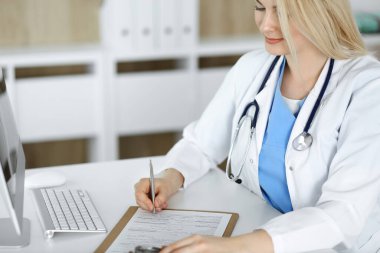 İş yerindeki bilinmeyen kadın-doktor klinikte ilaç geçmişi formunu dolduruyor, panonun yakın çekimini yapıyor.