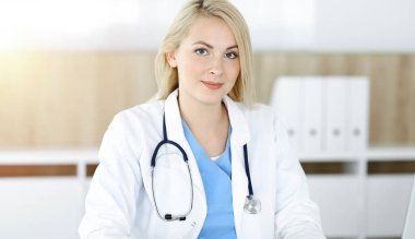 Güneşli klinikte masa başında oturan kadın doktor. Sarışın, neşeli doktor ilaç geçmişi formunu dolduruyor.