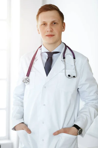 Man-dokter staat recht in een zonnige kliniek. Geneesmiddelenconcept — Stockfoto
