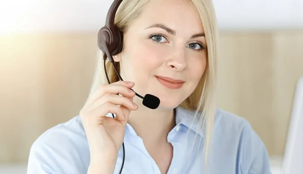 Blond affärskvinna sitter och kommuniceras med headset i call center i soligt kontor. Begreppet telehandel — Stockfoto