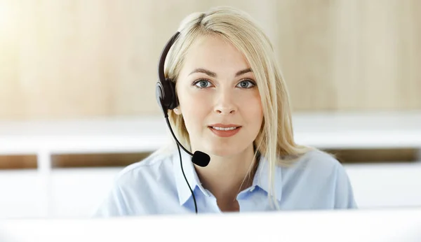 Blond affärskvinna sitter och kommuniceras med headset i call center i soligt kontor. Begreppet telehandel — Stockfoto