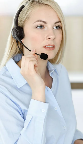 Mulher de negócios loira sentada e comunicada por fone de ouvido no escritório do call center ensolarado — Fotografia de Stock