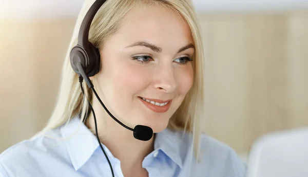 Blonde business woman sitting and communicated by headset in call center in sunny office. Concept of telesales business Stock Image