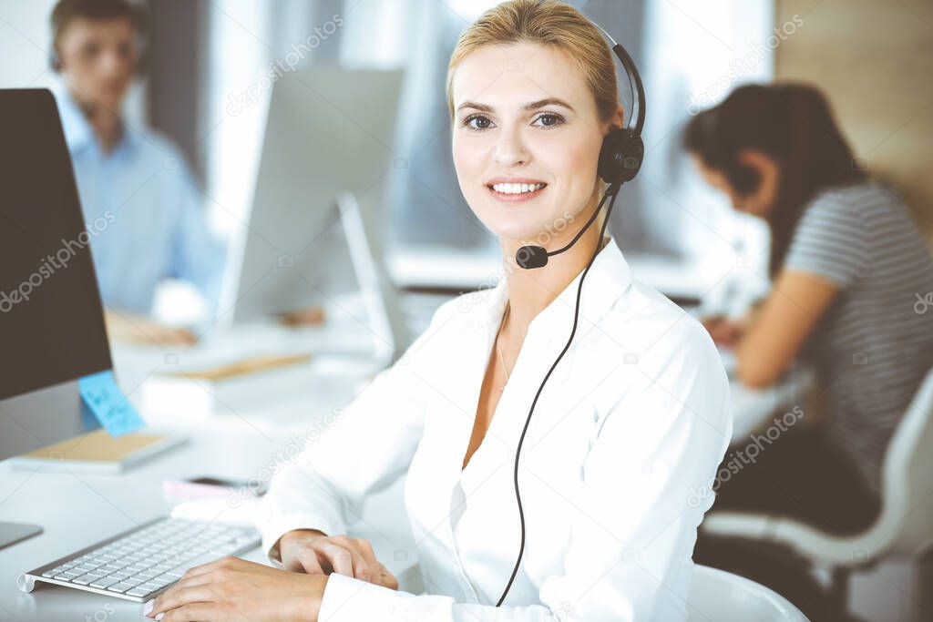 Blonde business woman using headset for communication and consulting people at customer service office. Call center. Group of operators at work