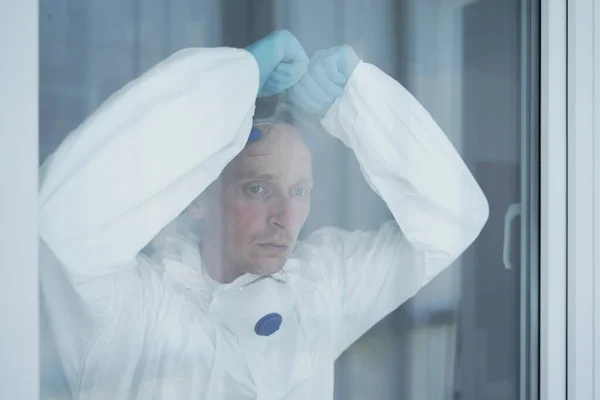 Yüzü morarmış ve Yüzü Yüzü Maskeli Erkek Hemşire Pencereden Dışarı Bakıyor.