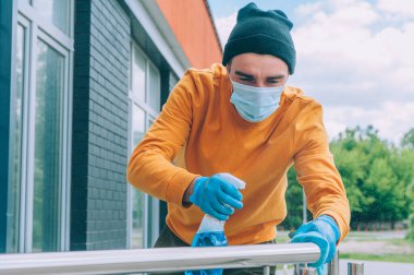 Genç bir adam elinde bez parçasıyla mavi bir antiseptik ile tırabzanı dezenfekte ediyor. COVID-19 'dan koruma ve önleme