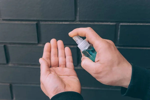 Man disinfecting his hands with blue hand sanitizer from a bottle on brick background