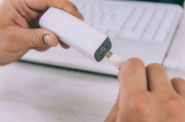 Adam, taşınabilir şarj cihazını dizüstü bilgisayarla şarj ediyor.