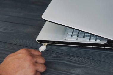 Beyaz dizüstü bilgisayara ahşap arka planda kablo tutun.