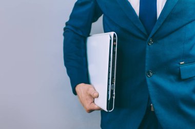 Elinde dizüstü bilgisayarla gri arka planda mavi ceketli bir iş adamı.