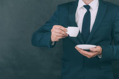 Elinde kahveyle arka planda koyu renk ceketli bir iş adamı.