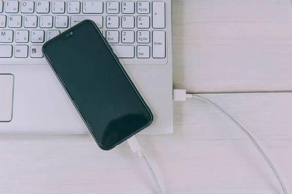 Akıllı Telefon Beyaz Ahşap Bir Masada Dizüstü Bilgisayardan Şarj Oluyor — Stok fotoğraf